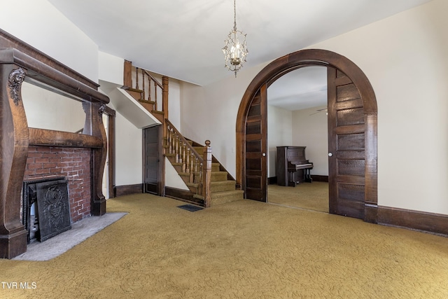 unfurnished living room featuring an inviting chandelier, light colored carpet, and a brick fireplace