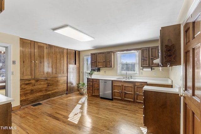 kitchen featuring dishwasher, light hardwood / wood-style flooring, wooden walls, and sink