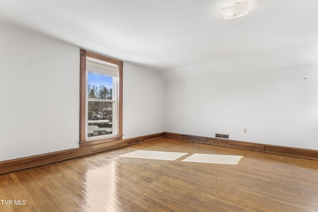 empty room with light wood-type flooring, basketball court, and vaulted ceiling