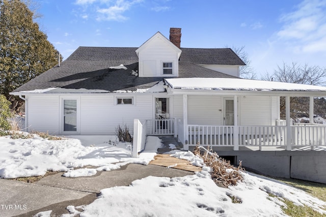 snow covered back of property featuring covered porch