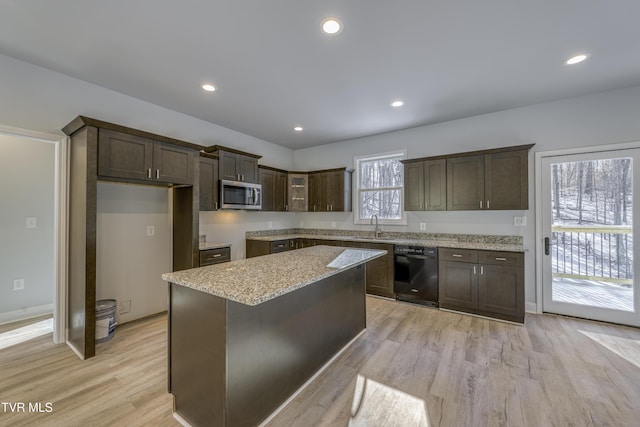 kitchen with dark brown cabinetry, black dishwasher, a kitchen island, light stone countertops, and light hardwood / wood-style floors