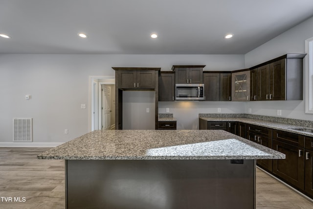 kitchen with light stone counters, dark brown cabinets, light hardwood / wood-style floors, and a kitchen island