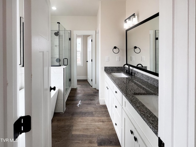 full bathroom featuring double vanity, a stall shower, wood finished floors, a soaking tub, and a sink