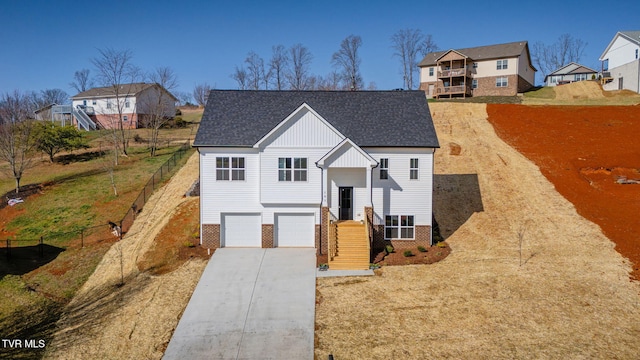 raised ranch with fence, roof with shingles, concrete driveway, a garage, and brick siding