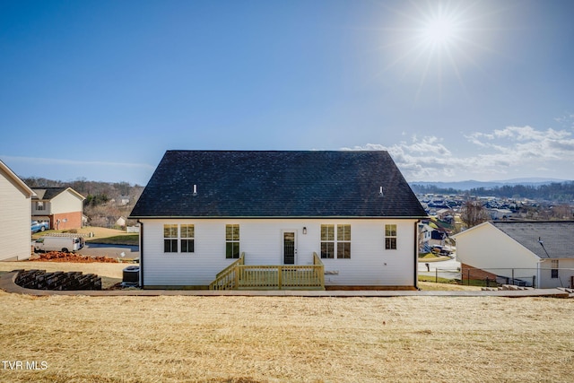 rear view of house with a wooden deck, roof with shingles, cooling unit, and fence