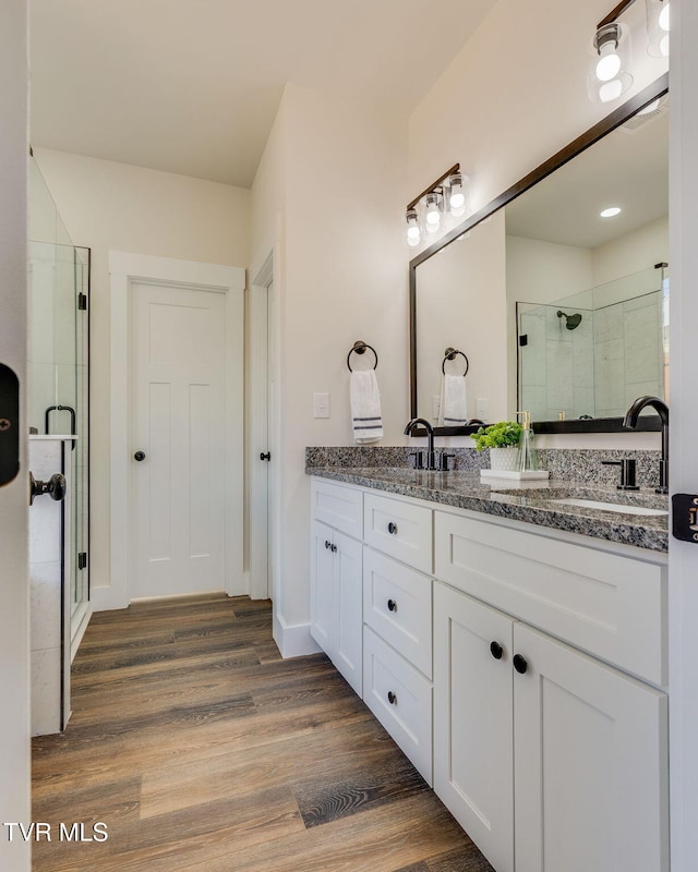 bathroom featuring double vanity, wood finished floors, a stall shower, and a sink