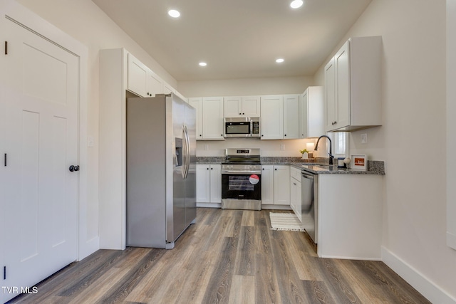 kitchen featuring white cabinets, wood finished floors, appliances with stainless steel finishes, and a sink