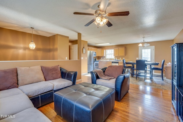 living room featuring light wood-type flooring, a textured ceiling, and ceiling fan with notable chandelier