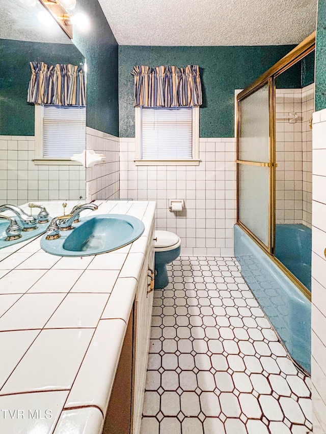 full bathroom with toilet, combined bath / shower with glass door, tile walls, and vanity