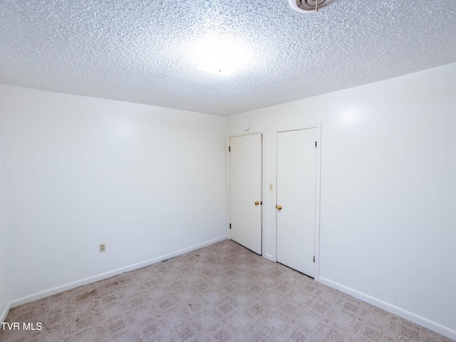 spare room featuring light colored carpet and a textured ceiling