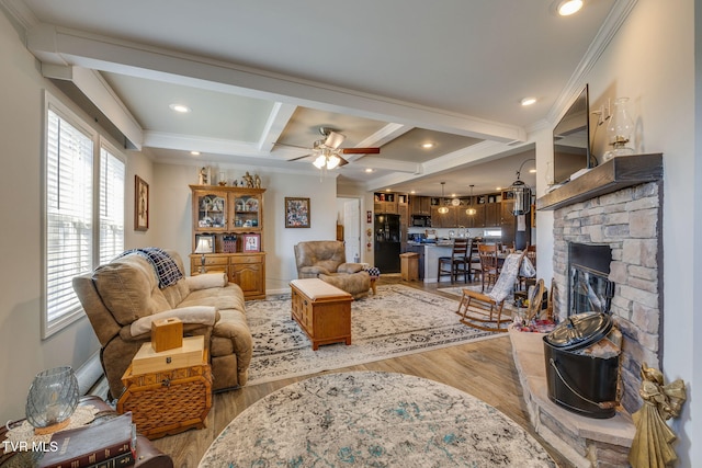 living room with a fireplace, ornamental molding, ceiling fan, light hardwood / wood-style flooring, and beam ceiling