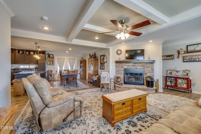 living room featuring crown molding, light wood-type flooring, beam ceiling, and a stone fireplace