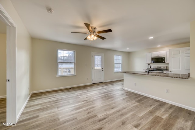 kitchen featuring ceiling fan, kitchen peninsula, stainless steel electric stove, white cabinets, and light stone counters