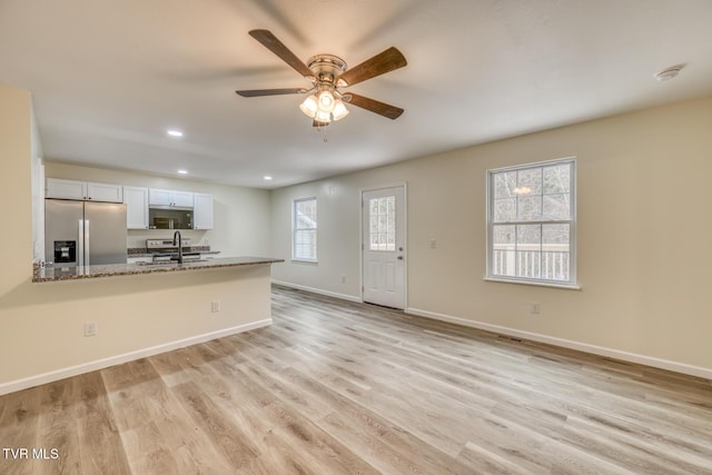 kitchen with baseboards, stainless steel fridge with ice dispenser, light wood-style flooring, a peninsula, and a sink