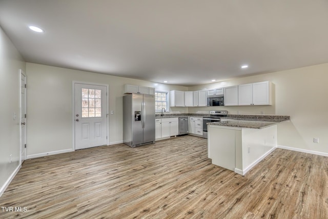 kitchen with kitchen peninsula, white cabinetry, light hardwood / wood-style flooring, appliances with stainless steel finishes, and dark stone counters