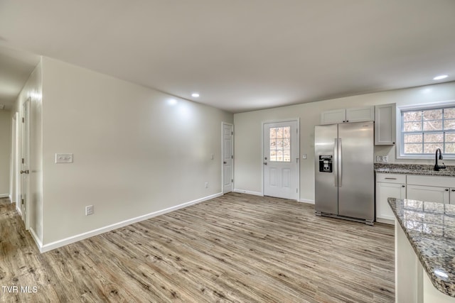 kitchen featuring stainless steel refrigerator with ice dispenser, light stone countertops, white cabinetry, and plenty of natural light