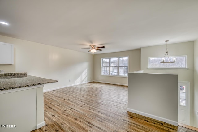 unfurnished living room featuring ceiling fan with notable chandelier and light hardwood / wood-style floors