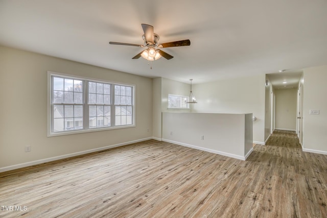 spare room with ceiling fan with notable chandelier and light hardwood / wood-style flooring