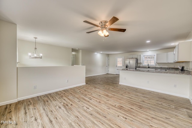 unfurnished living room with light wood-type flooring, ceiling fan with notable chandelier, and sink