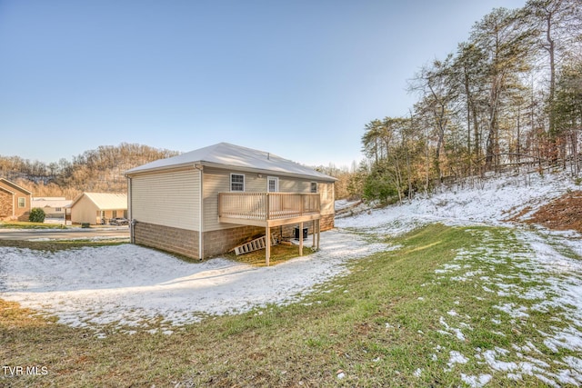 snow covered house featuring a deck and a yard