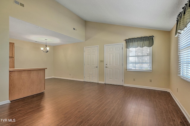 unfurnished room featuring a textured ceiling, dark wood-type flooring, lofted ceiling, and a notable chandelier