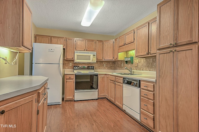 kitchen with white appliances, a textured ceiling, light brown cabinetry, sink, and light wood-type flooring