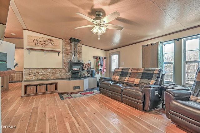 living room with ceiling fan, lofted ceiling, a wood stove, and light wood-type flooring