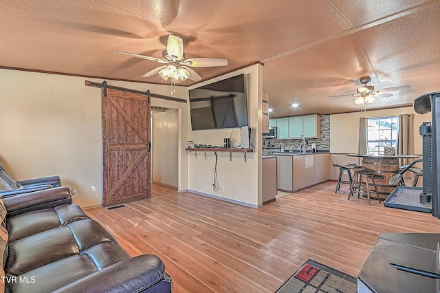 living room with a barn door, a textured ceiling, ceiling fan, and light hardwood / wood-style flooring