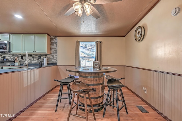 dining room with sink, crown molding, a textured ceiling, light hardwood / wood-style flooring, and ceiling fan