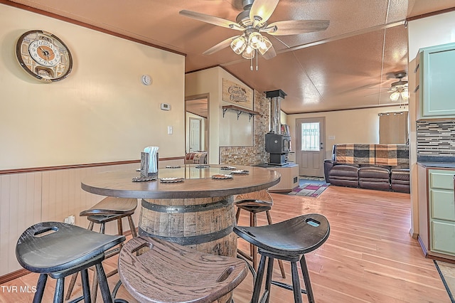 dining space with lofted ceiling, a wood stove, ceiling fan, and light wood-type flooring