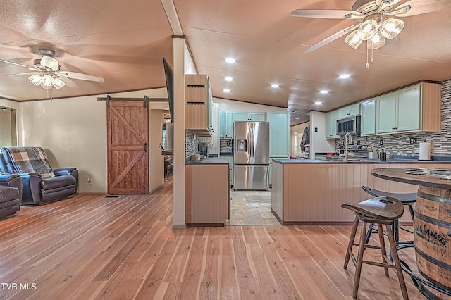 kitchen with appliances with stainless steel finishes, kitchen peninsula, ceiling fan, light hardwood / wood-style floors, and a barn door