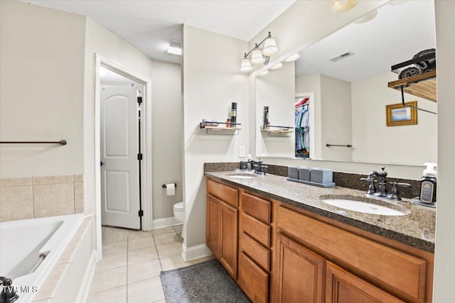 bathroom with tiled bath, toilet, vanity, and tile patterned flooring