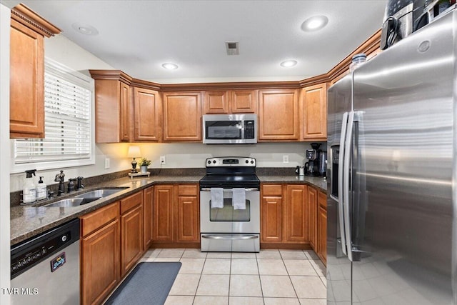 kitchen featuring light tile patterned floors, appliances with stainless steel finishes, dark stone counters, and sink