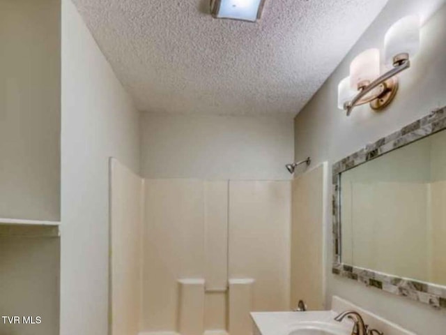 bathroom with a textured ceiling, a shower, and vanity