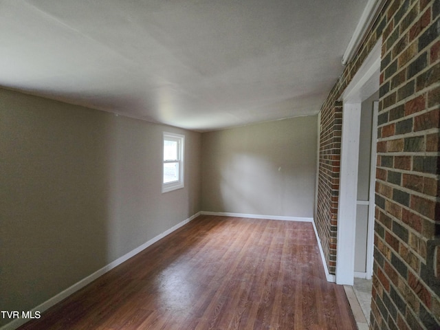 empty room with brick wall and wood-type flooring