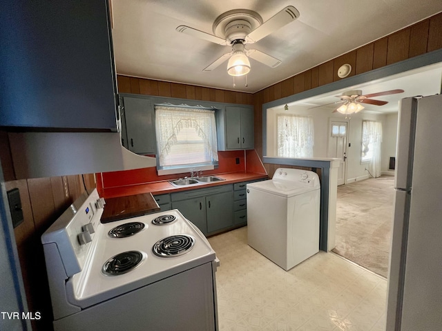 kitchen with stainless steel fridge, washer / dryer, sink, white electric range oven, and wood walls