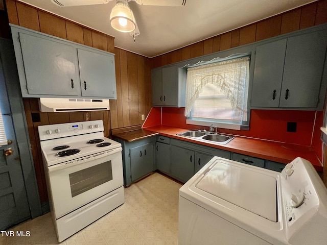 kitchen featuring sink, electric range, wooden walls, and independent washer and dryer