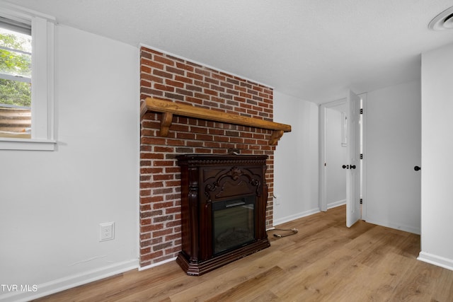 unfurnished living room featuring a textured ceiling, a brick fireplace, and light hardwood / wood-style floors