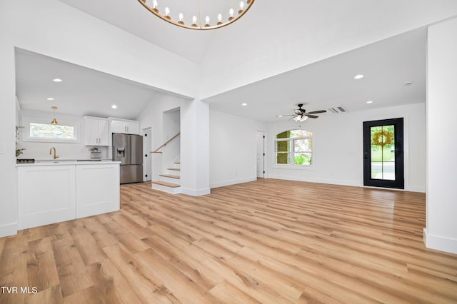 unfurnished living room with recessed lighting, light wood-style flooring, vaulted ceiling, baseboards, and stairs