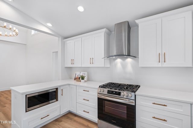 kitchen with light countertops, appliances with stainless steel finishes, vaulted ceiling, wall chimney range hood, and a peninsula