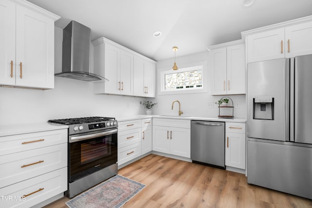 kitchen with lofted ceiling, a sink, white cabinets, appliances with stainless steel finishes, and wall chimney exhaust hood