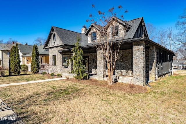 view of front facade with a porch, stone siding, roof with shingles, a chimney, and a front yard