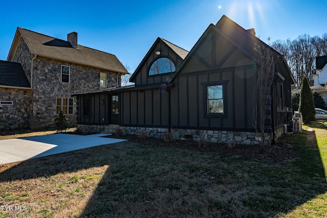 rear view of property featuring a patio, stone siding, a chimney, a yard, and board and batten siding