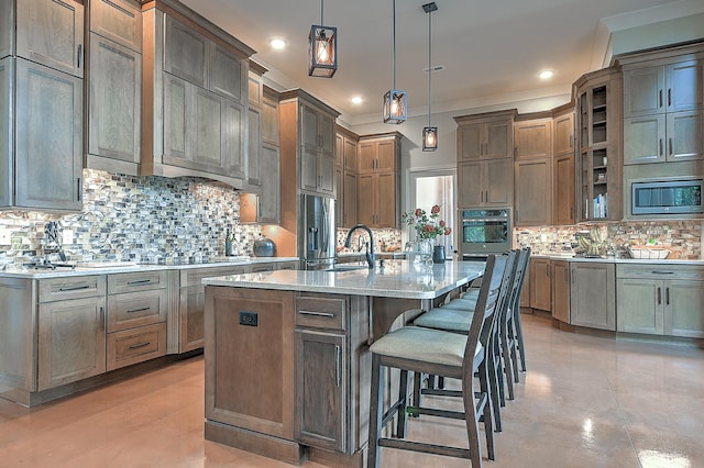 kitchen featuring pendant lighting, a kitchen island with sink, stainless steel appliances, and tasteful backsplash