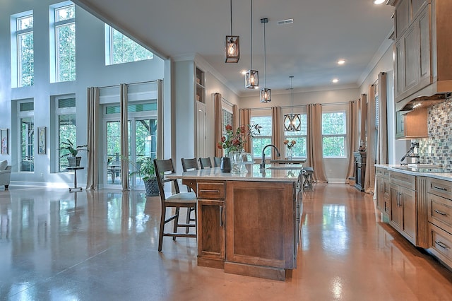 kitchen featuring a kitchen bar, a center island with sink, backsplash, decorative light fixtures, and crown molding