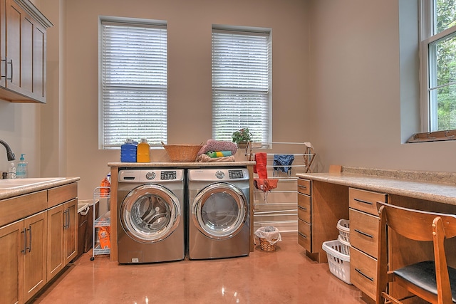 clothes washing area with washer and clothes dryer, sink, a healthy amount of sunlight, and cabinets