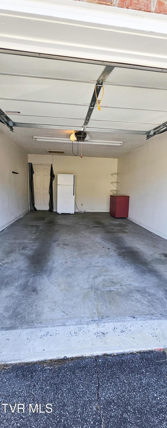 garage featuring white refrigerator and a garage door opener