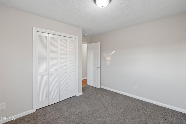 unfurnished bedroom featuring a textured ceiling, a closet, and dark colored carpet