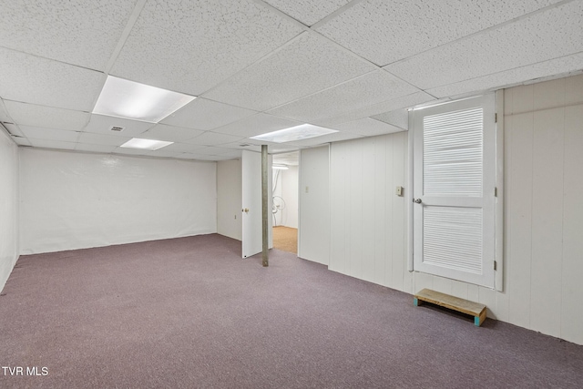 basement with dark colored carpet, a drop ceiling, and wooden walls