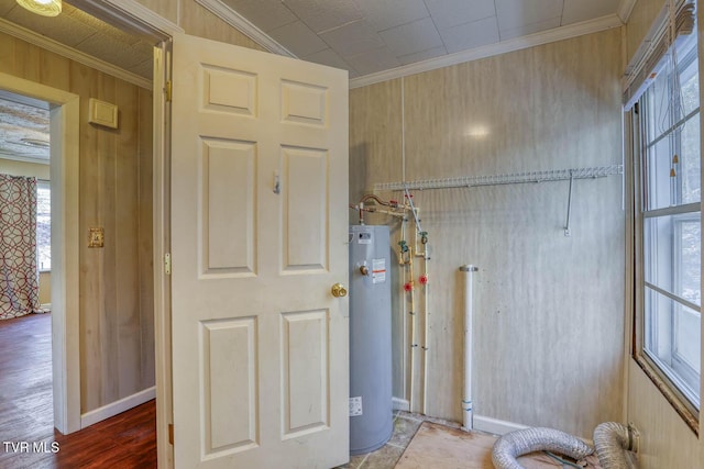 clothes washing area with crown molding, wood walls, and water heater